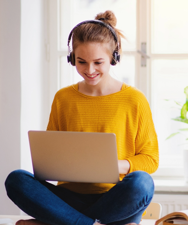 Woman sitting cross-legged on table with laptop and headphones