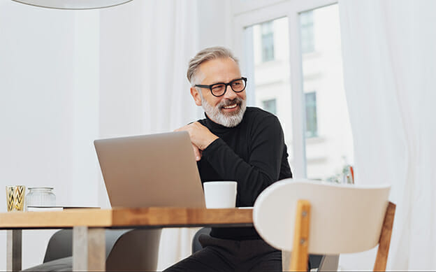 smiling man sitting at desk in front of his laptop