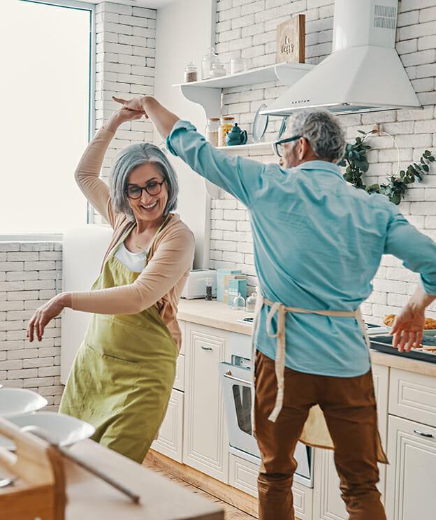 Older couple dancing happily in the kitchen.