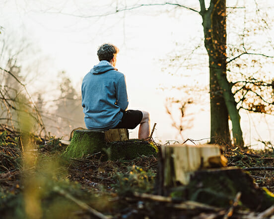 Mann sitzt auf einem Baumstamm im Wald