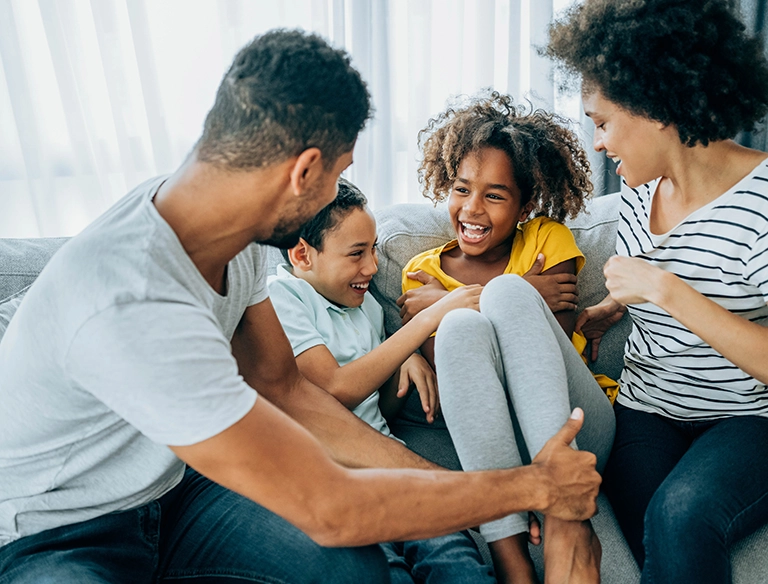 Glückliche Familie mit Eltern und Kindern sitzt lachend auf Sofa