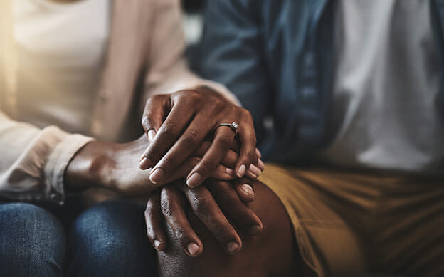 Bildausschnitt eines Mannes und einer Frau, die auf einem Sofa sitzen und sich an den Händen halten