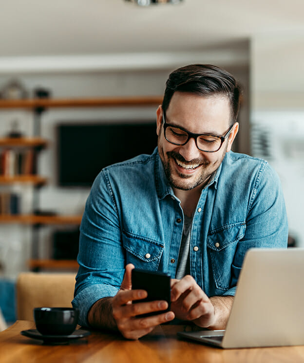 Ein fröhlicher Mann, der zu Hause ein Smartphone benutzt.