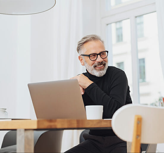 smiling man sitting at desk in front of his laptop