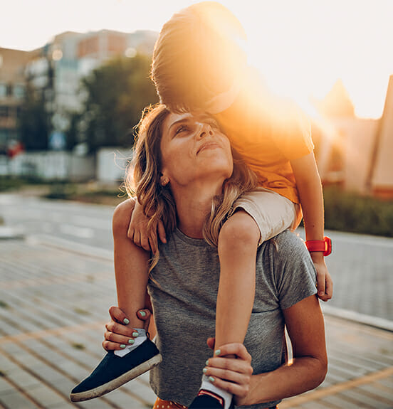 Mother carrying son on shoulder in sunset