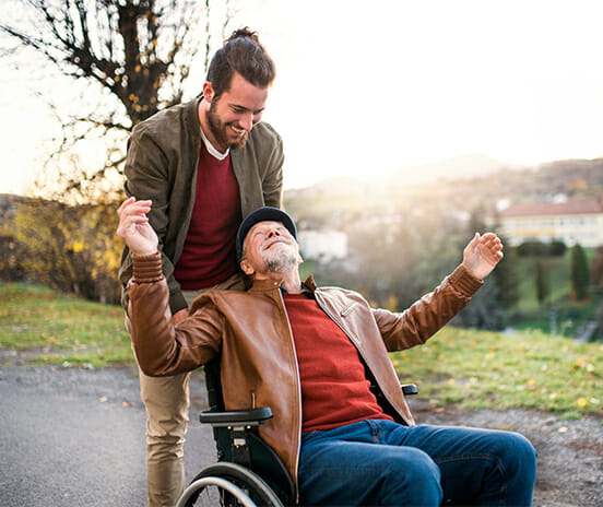 Junger Mann und sein älterer Vater im Rollstuhl auf einem Spaziergang