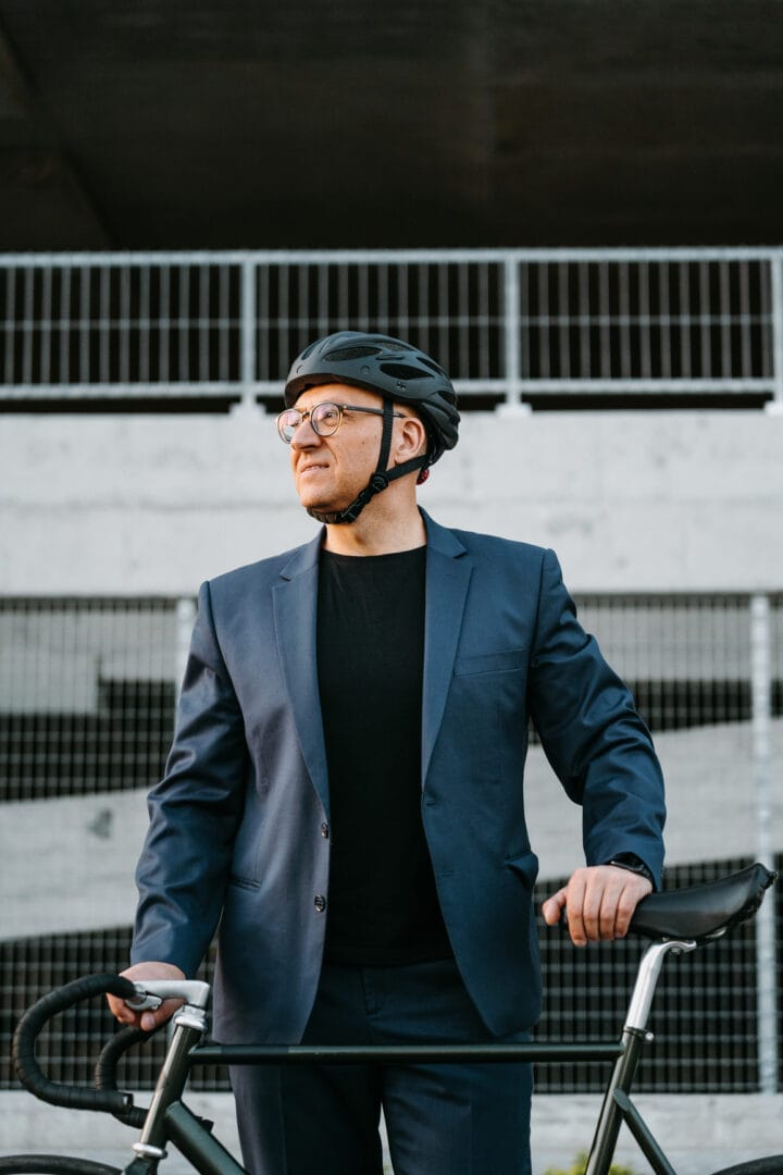 Mann mittleren Alters in Anzug und mit Fahrradhelm steht vor zufrieden vor seinem Rennrad –Symbolbild für Coaching für Führungskräfte