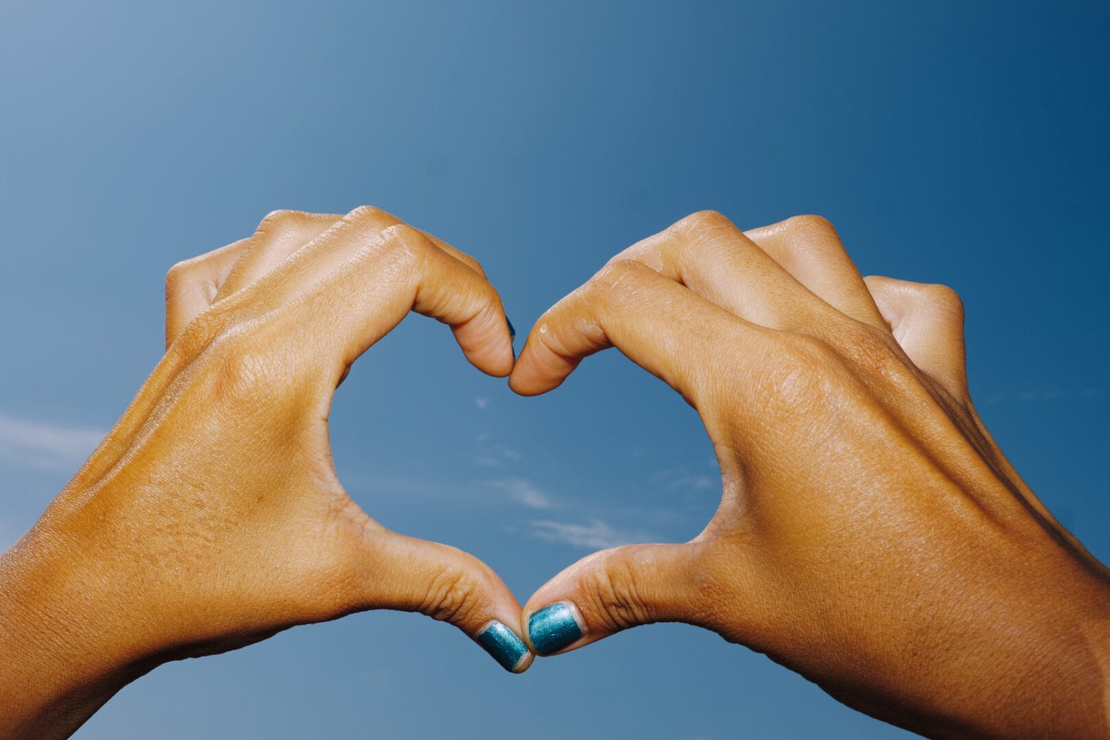 Hände formen Herz vor blauem Himmel